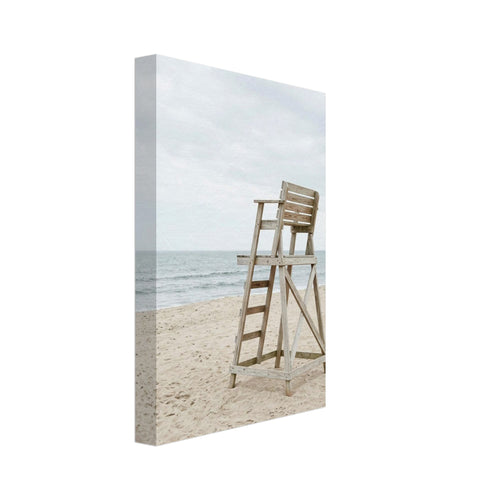 Empty wooden lifeguard chair on pale sand beside gentle sea waves beneath an overcast sky.