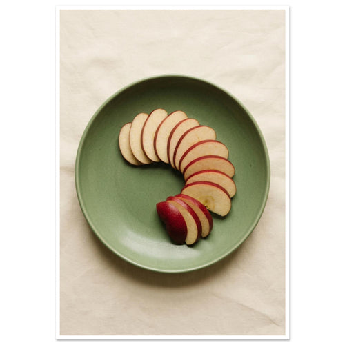 Red-skinned apple slices arranged in a curve on a green plate, photographed from above on cream fabric.