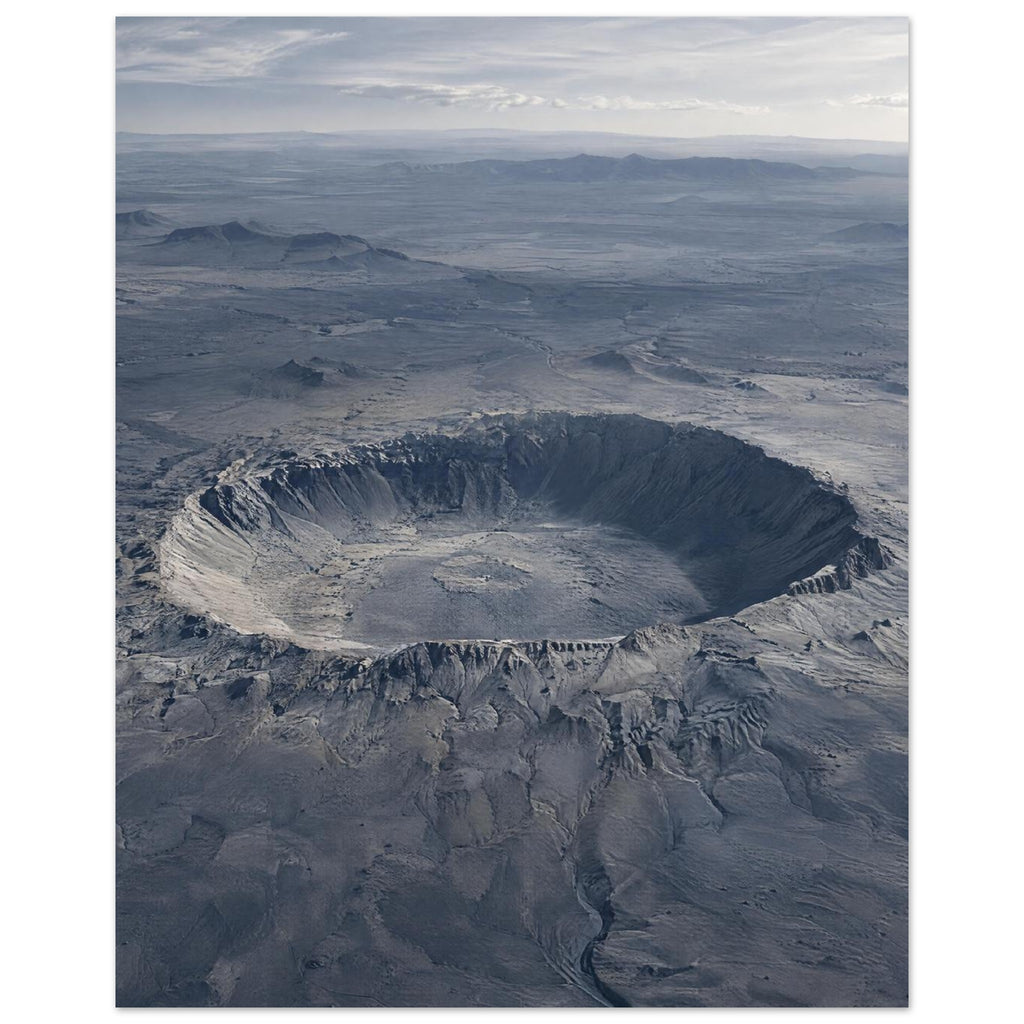 Large circular crater in a blue-grey desert plain, with rugged slopes, distant hills and a cloudy sky.