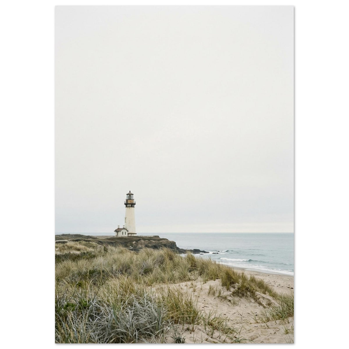 Lighthouse on a rocky headland beyond grassy sand dunes, with gentle waves and a wide, pale grey sky.