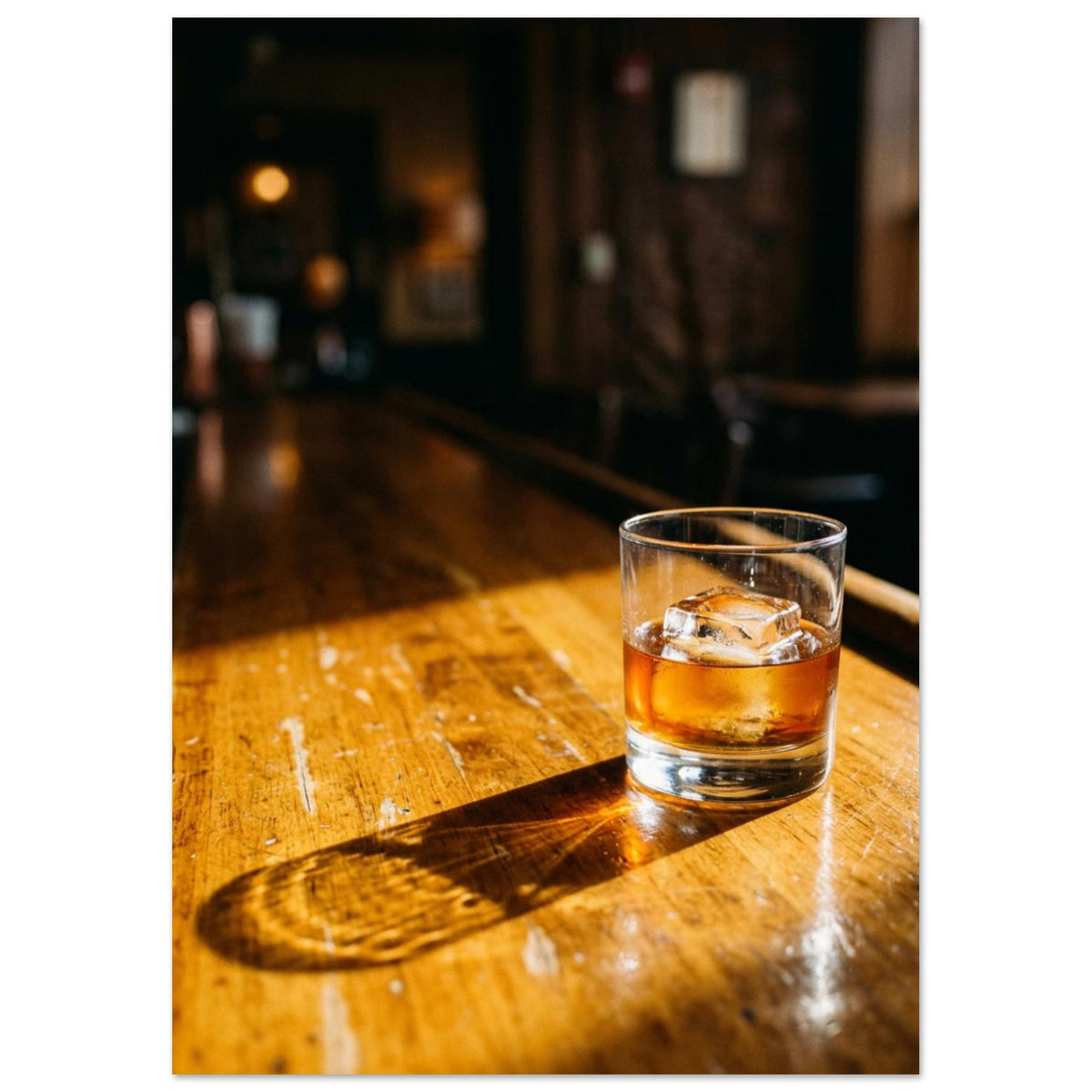Tumbler of amber drink with ice on a sunlit wooden bar, casting a long shadow against a dark, blurred interior.