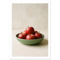 Three red apples nestled in folds of green fabric on a pale wooden surface, with soft light and shadows.