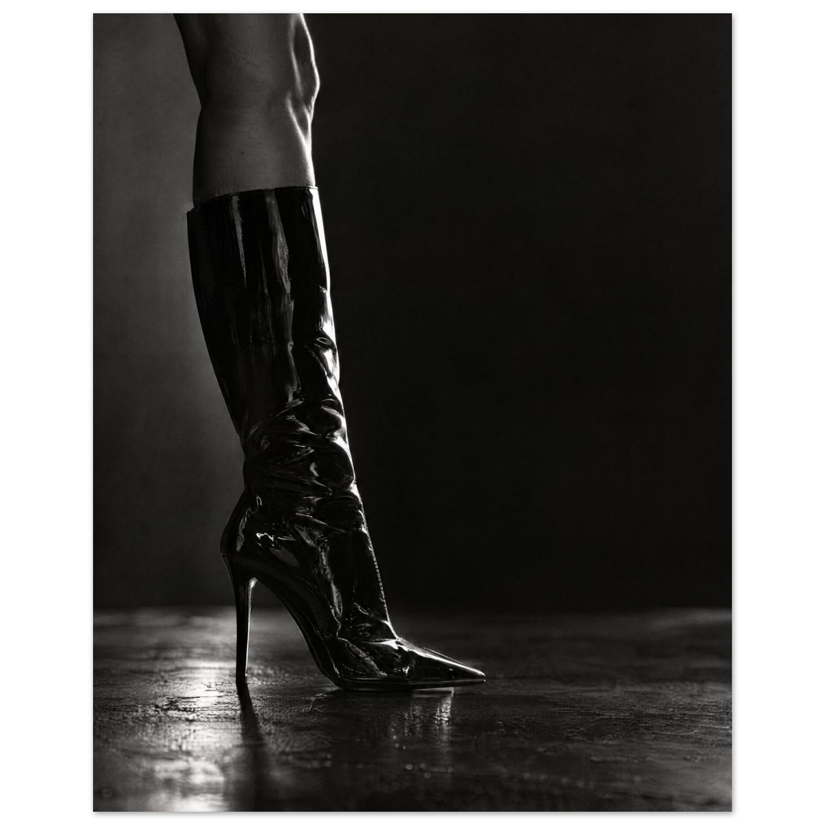 Black and white photograph of a leg in a glossy knee-high stiletto boot on a reflective floor against a dark backdrop.