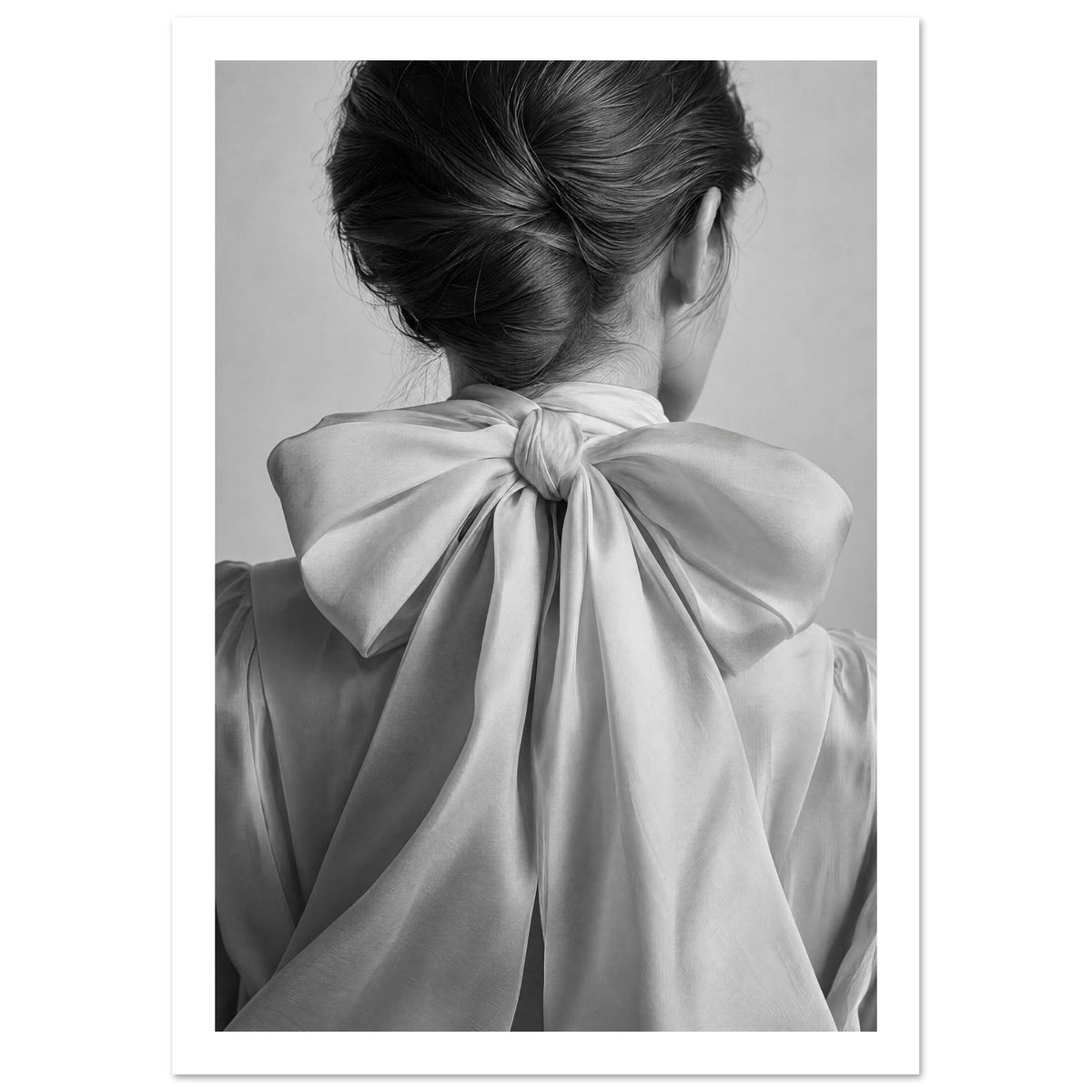 Woman seen from behind with swept-up dark hair and a large pale fabric bow tied at her nape, in black and white.
