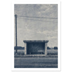 Rural bus shelter with an empty bench beside a road, open fields and a utility pole beneath a textured blue-grey sky.