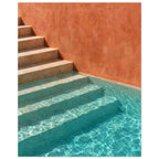 Stone steps descending into turquoise pool water beside a terracotta wall, with sunlight rippling across submerged stairs.