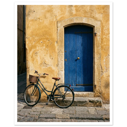Green bicycle with a woven basket beside a blue wooden door in a golden plaster wall, above worn stone paving.