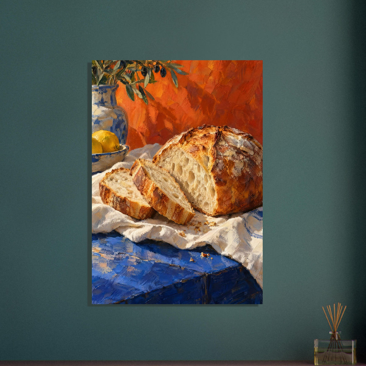 Sliced crusty loaf on cream cloth over a blue table, with lemons, pottery and olive branches against an orange backdrop.