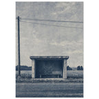 Rural bus shelter with an empty bench beside a road, open fields and a utility pole beneath a textured blue-grey sky.