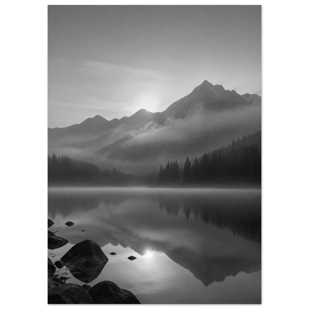 Mountain peaks and conifer forests reflected in a misty lake, with rocks in the foreground, in black and white.