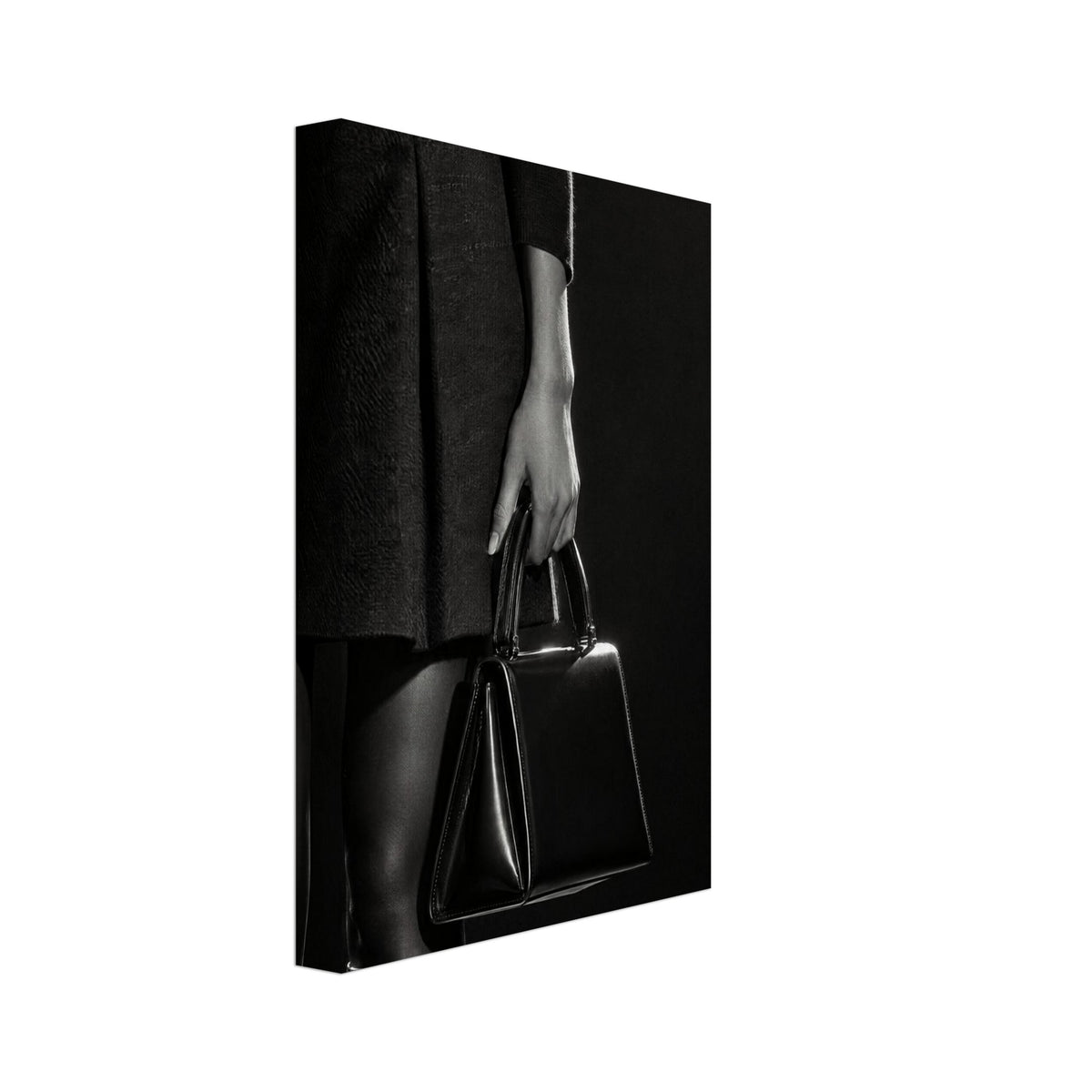 Cropped black and white photograph of a figure in a dark skirt and boots holding a glossy structured handbag.