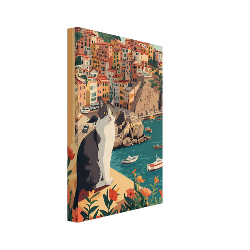 Grey and white cat on a flower-lined ledge above a teal harbour, small boats and colourful hillside buildings.