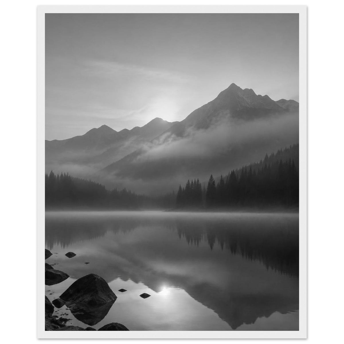 Mountain peaks and conifer forests reflected in a misty lake, with rocks in the foreground, in black and white.