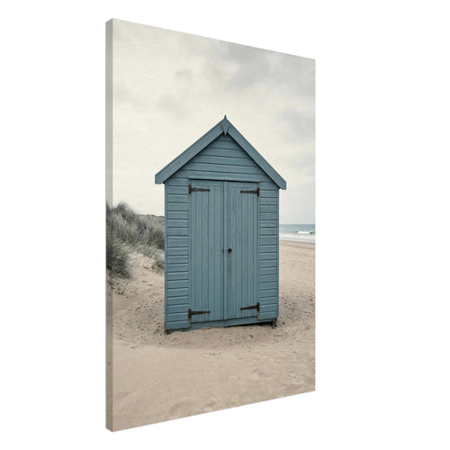 Blue wooden beach hut with closed doors on pale sand, with dune grasses, sea waves and an overcast sky.