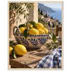 Lemons in a blue-and-white bowl on a wooden table, with olive branches, checked cloth and a coastal village beyond.