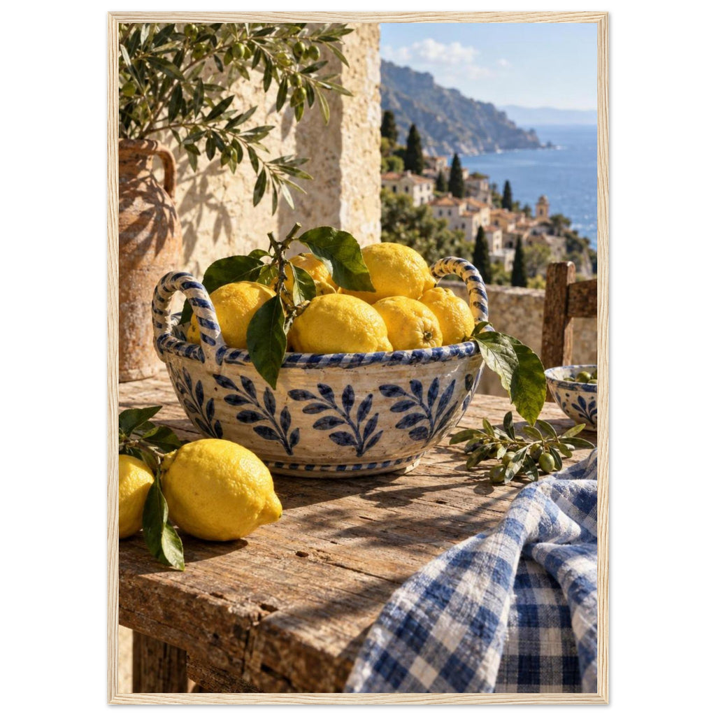 Lemons in a blue-and-white bowl on a wooden table, with olive branches, checked cloth and a coastal village beyond.