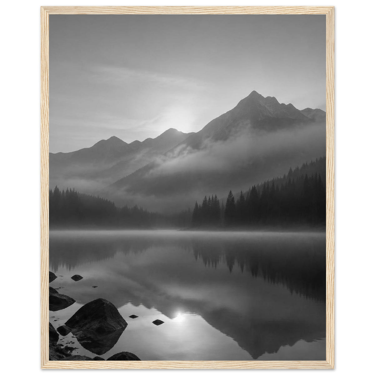 Mountain peaks and conifer forests reflected in a misty lake, with rocks in the foreground, in black and white.