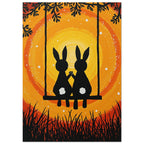 Two black rabbits with white tails hold paws on a swing, surrounded by branches and grass against yellow and orange swirls.