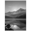 Mountain peaks and conifer forests reflected in a misty lake, with rocks in the foreground, in black and white.