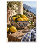 Lemons in a blue-and-white bowl on a wooden table, with olive branches, checked cloth and a coastal village beyond.