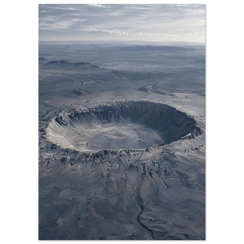Large circular crater in a blue-grey desert plain, with rugged slopes, distant hills and a cloudy sky.