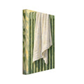 White towel draped over a green ribbed radiator against a yellow wall, with a leafy plant and soft shadows.