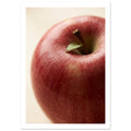 Close-up of a red apple with mottled skin, a brown stalk and a small green leaf against a soft cream background.