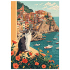Grey and white cat on a flower-lined ledge above a teal harbour, small boats and colourful hillside buildings.