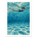Swimmer in a dark blue swimsuit beneath rippling turquoise water, with bubbles and pale light patterns across the pool floor.