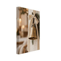Golden bell hanging from a cream bow on a wooden peg, with evergreen sprigs and blurred candlelight behind.
