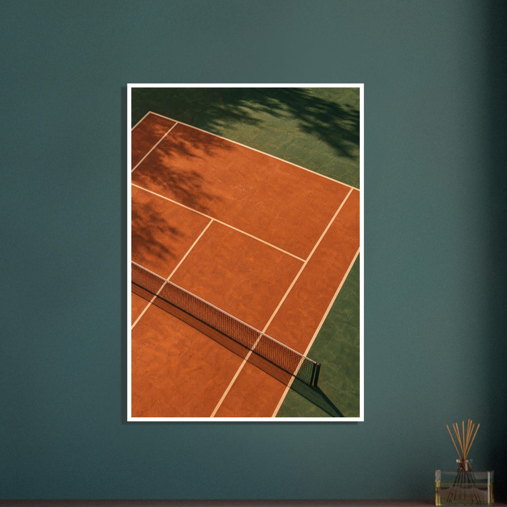 Terracotta tennis court viewed from above, with green surrounds, pale lines, a dark net and tree shadows.