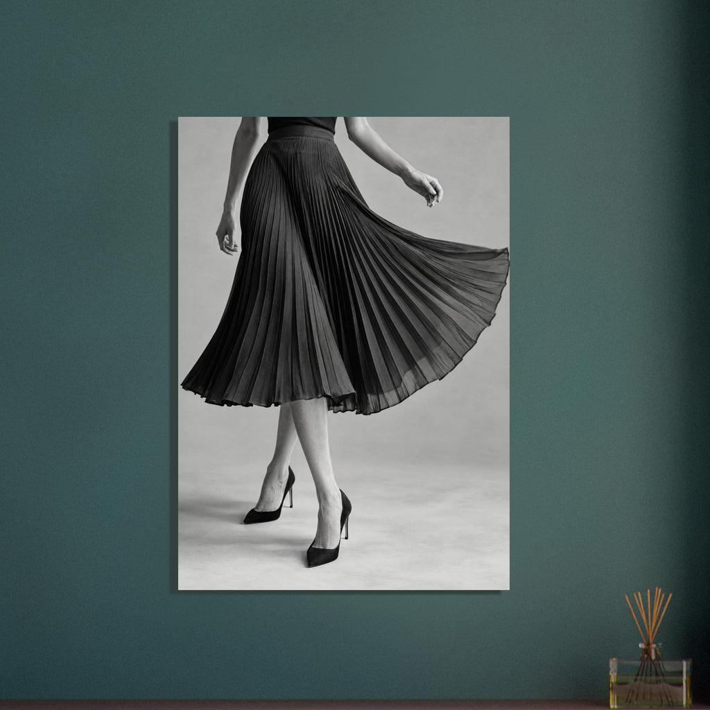 Cropped figure in a flowing black pleated skirt and pointed high heels, with crossed legs against a grey background.