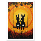 Two black rabbits with white tails hold paws on a swing, surrounded by branches and grass against yellow and orange swirls.