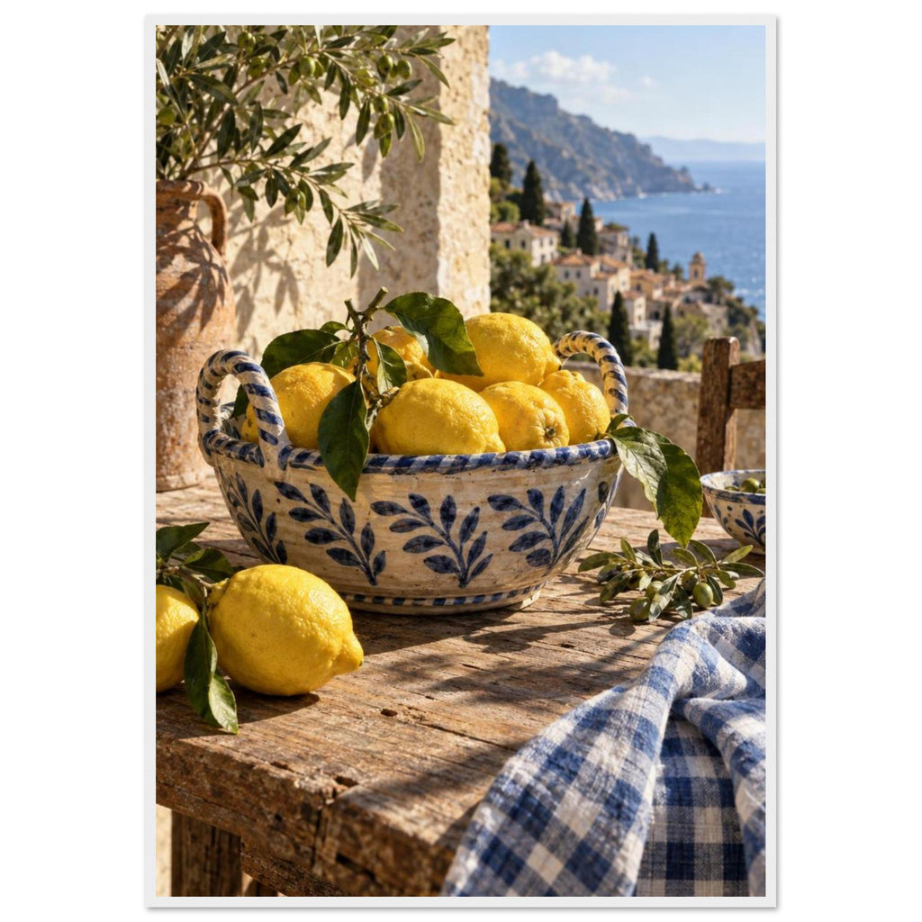 Lemons in a blue-and-white bowl on a wooden table, with olive branches, checked cloth and a coastal village beyond.