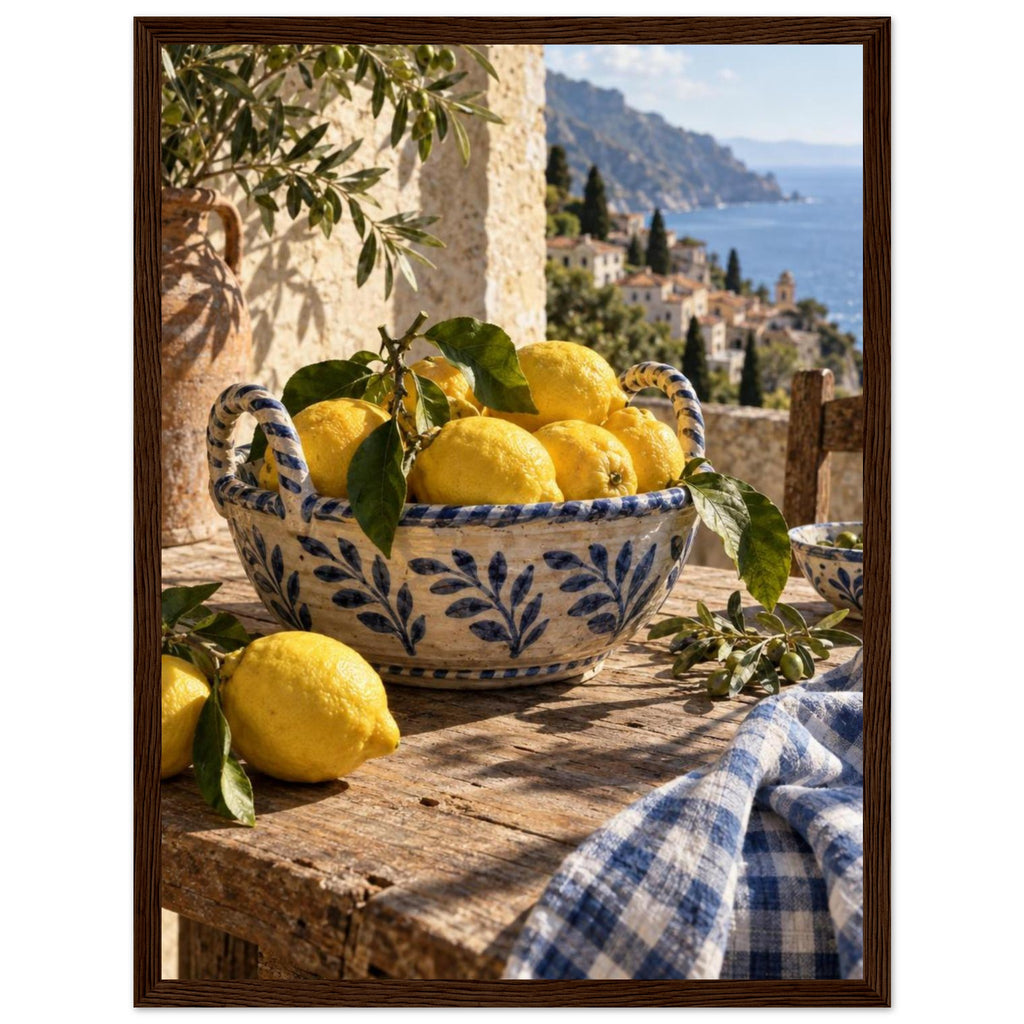 Lemons in a blue-and-white bowl on a wooden table, with olive branches, checked cloth and a coastal village beyond.