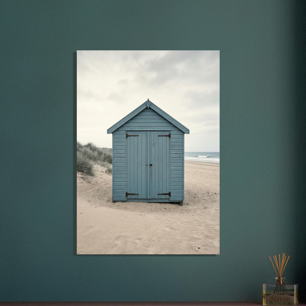 Blue wooden beach hut with closed doors on pale sand, with dune grasses, sea waves and an overcast sky.