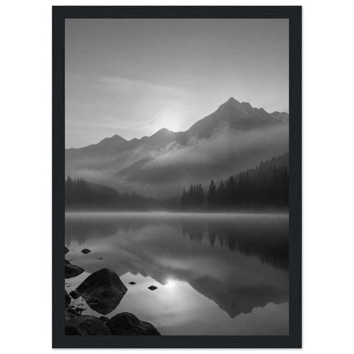 Mountain peaks and conifer forests reflected in a misty lake, with rocks in the foreground, in black and white.