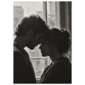 Black and white photograph of a couple touching foreheads beside a window, their profiles softly outlined by daylight.