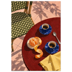 Two blue coffee cups, a peeled orange, spoon and yellow cloth on a red table beside a green woven chair and pink tiles.