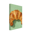 Golden-brown croissant with flaky layers and a deep green shadow on a textured mint green background.