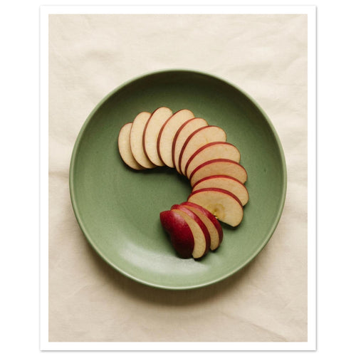 Red-skinned apple slices arranged in a curve on a green plate, photographed from above on cream fabric.