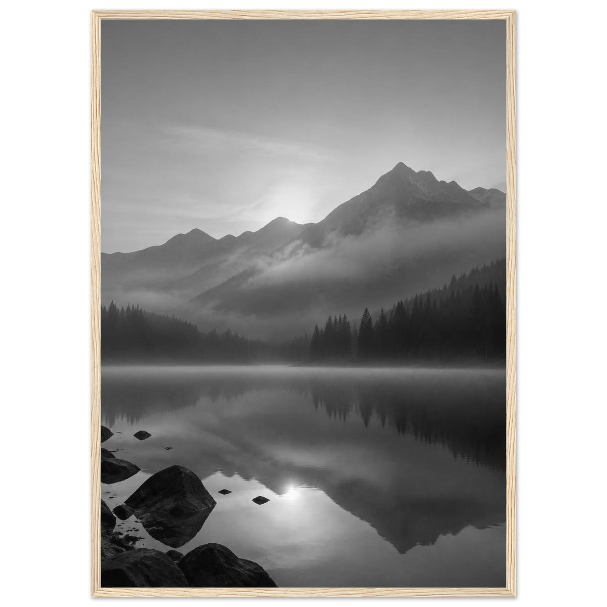 Mountain peaks and conifer forests reflected in a misty lake, with rocks in the foreground, in black and white.