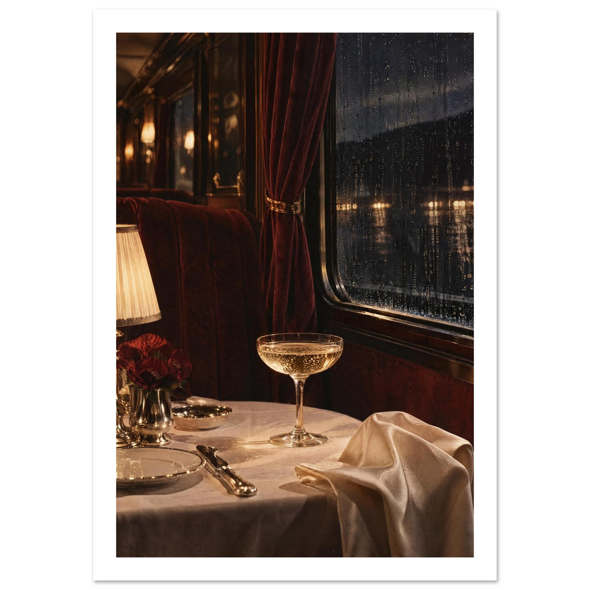 Train dining table with a coupe glass, glowing lamp and cream linen beside burgundy seating and a rain-streaked window.