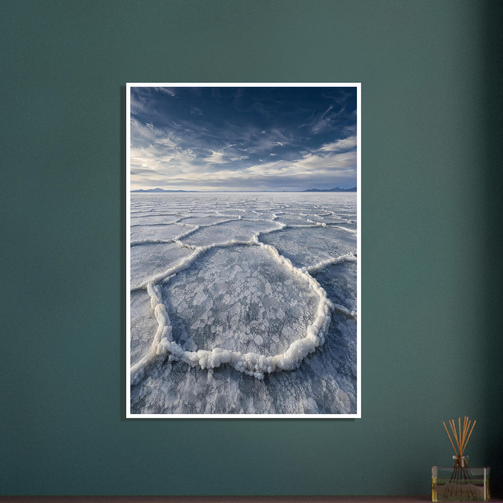 Salt flats with raised polygon-shaped ridges stretching towards distant mountains beneath a blue, cloud-streaked sky.