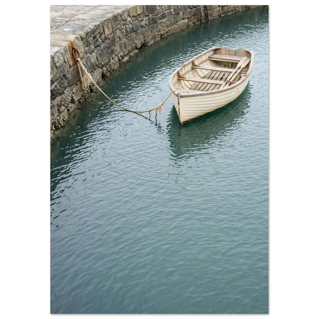 Cream wooden rowboat with oars, tied to a stone harbour wall above gently rippling blue-green water.