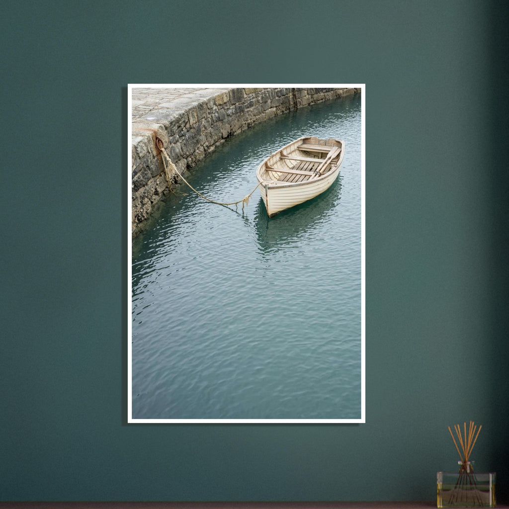 Cream wooden rowboat with oars, tied to a stone harbour wall above gently rippling blue-green water.