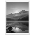 Mountain peaks and conifer forests reflected in a misty lake, with rocks in the foreground, in black and white.