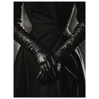 Overlapping hands in long black leather gloves against a dark fitted outfit, photographed in black and white.
