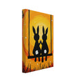 Two black rabbits with white tails hold paws on a swing, surrounded by branches and grass against yellow and orange swirls.