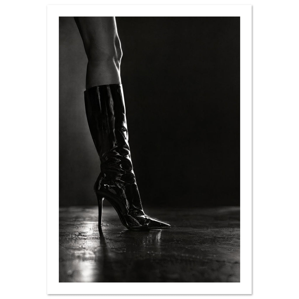 Black and white photograph of a leg in a glossy knee-high stiletto boot on a reflective floor against a dark backdrop.